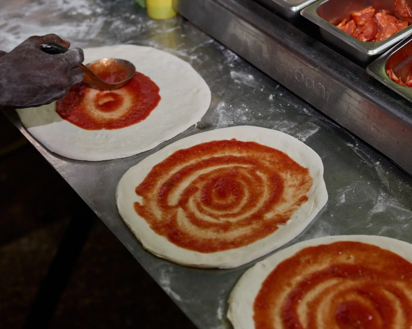 Tomato sauce being spread on dough